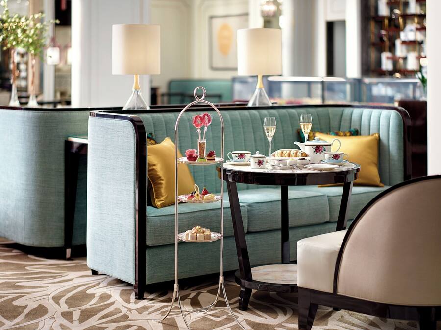 A seating area with a green sofa, a small round table with a tea set, and a decorative stand with flowers.