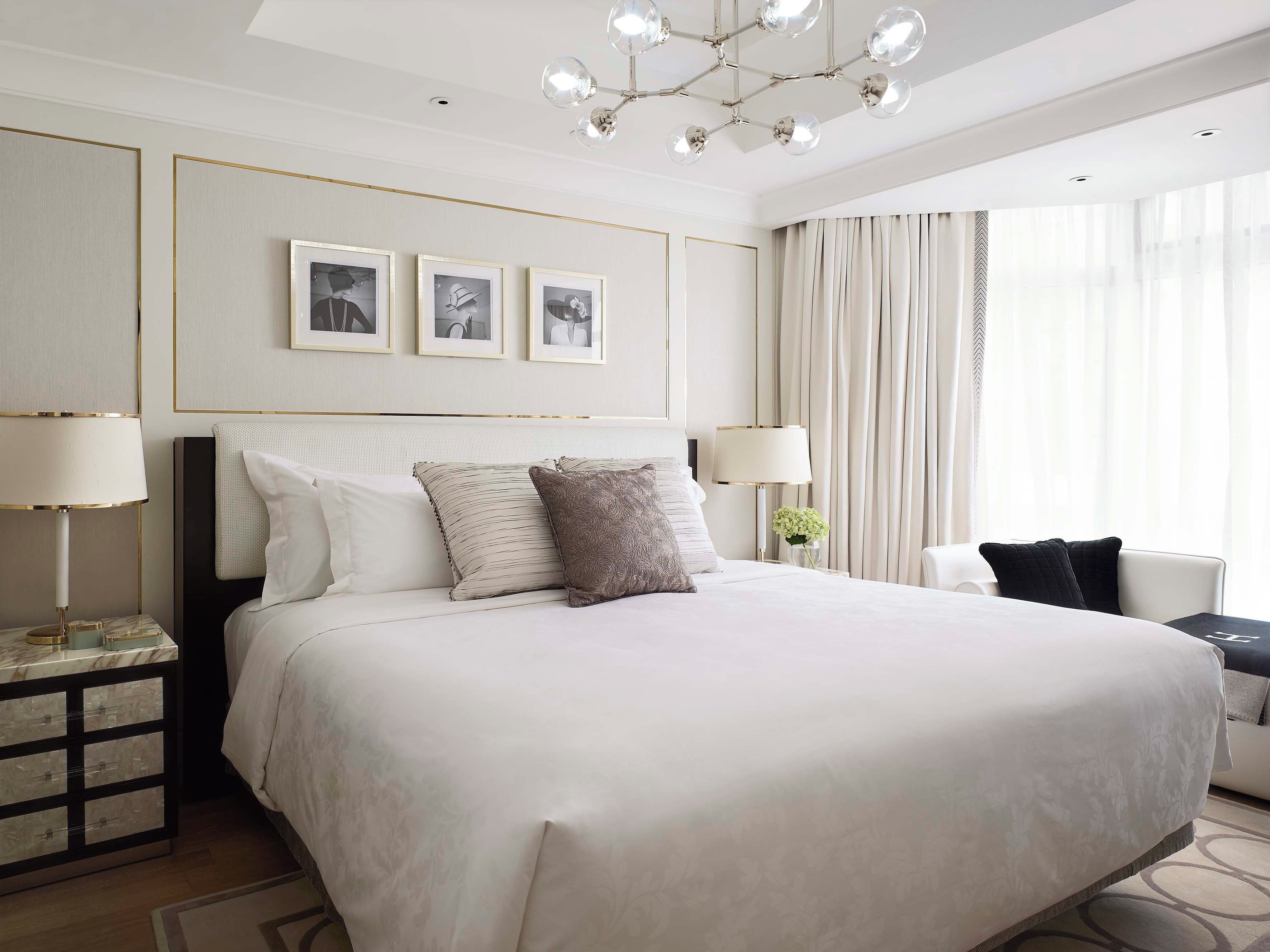 A hotel room with a large bed, bedside lamps, a nightstand, a dresser, and a chandelier.