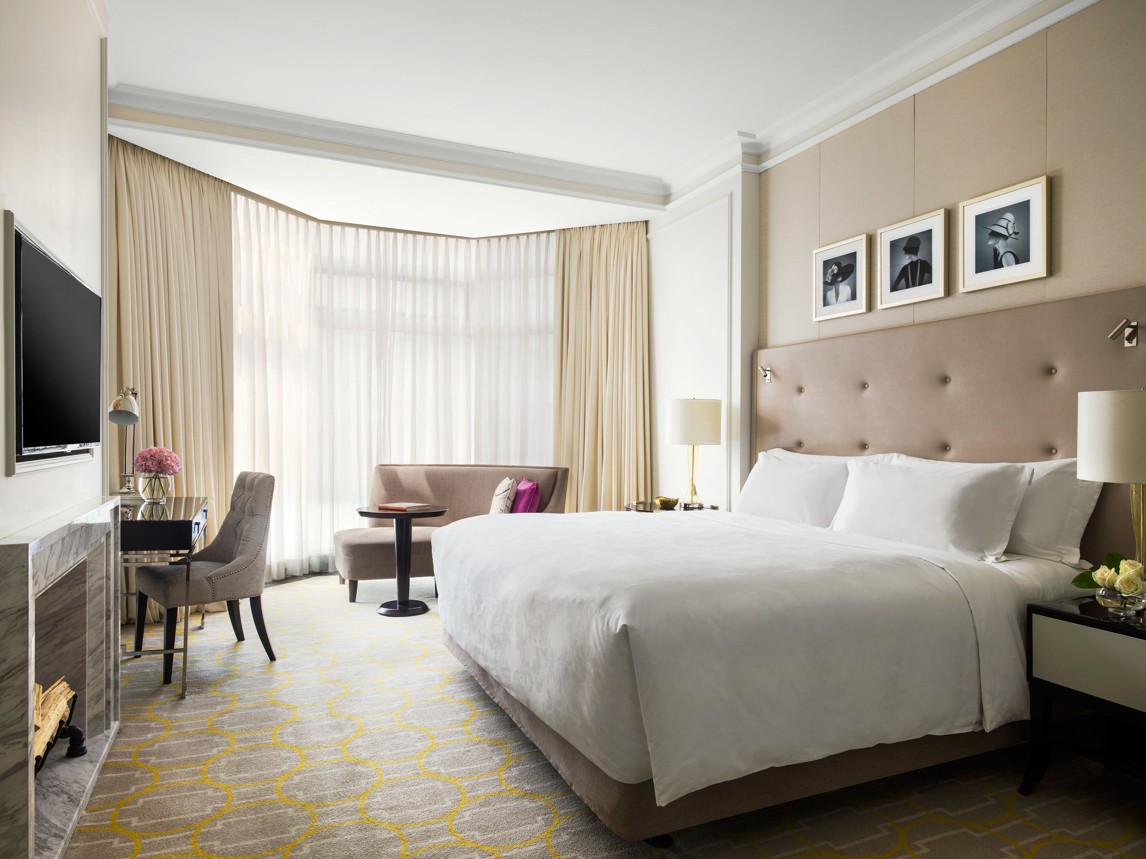 A hotel room with a large bed, a desk with a TV, a chair, and a view of the outdoors.