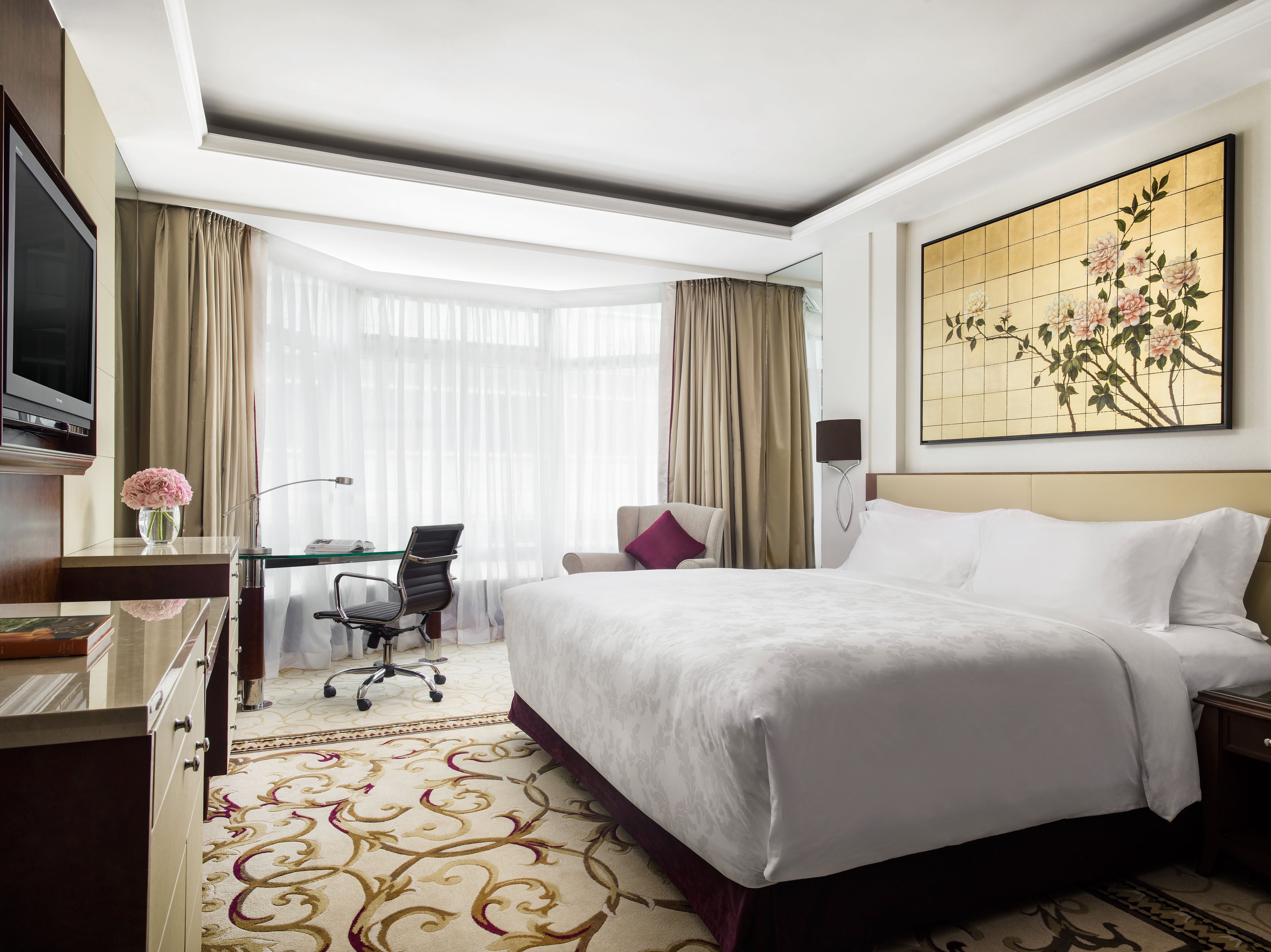 A hotel room with a large bed, a desk with a chair, a television, and a painting on the wall.