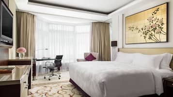 A hotel room with a large bed, a desk with a chair, a television, and a painting on the wall.