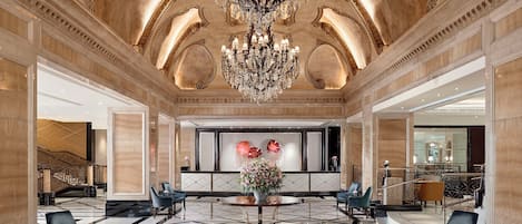A grand lobby with a large chandelier, marble flooring, and elegant seating arrangements.