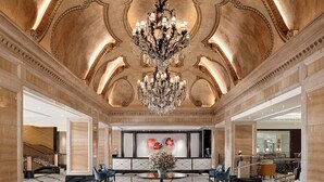 A grand lobby with a large chandelier, marble flooring, and elegant seating arrangements.