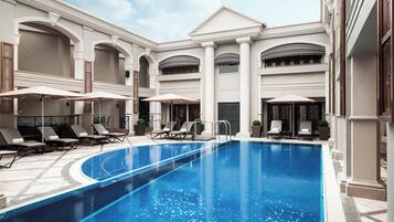 A swimming pool with lounge chairs and umbrellas, surrounded by a building with arches and columns.