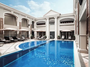 A swimming pool with lounge chairs and umbrellas, surrounded by a building with arches and columns. - The Langham, Hong Kong (Kowloon)
