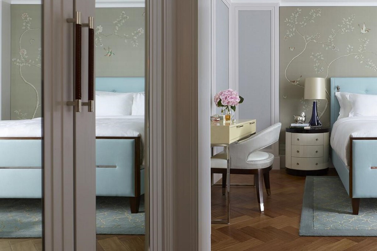 A hotel room with two beds, a desk, a chair, a nightstand, and a lamp.