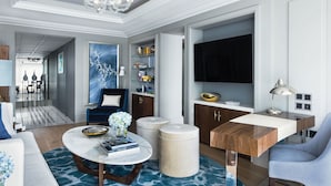 A modern living room with a chandelier, a television, a coffee table with books, and a blue sofa. - The Langham, Hong Kong (Kowloon)