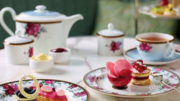 A tea setting with floral-patterned tableware, including a teapot, cups, and plates, with a dessert on a floral plate.