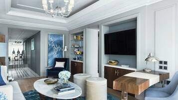 Un salon moderne avec un lustre, une grande peinture abstraite bleue, un canapé bleu, une table basse avec des livres et un téléviseur fixé au mur.