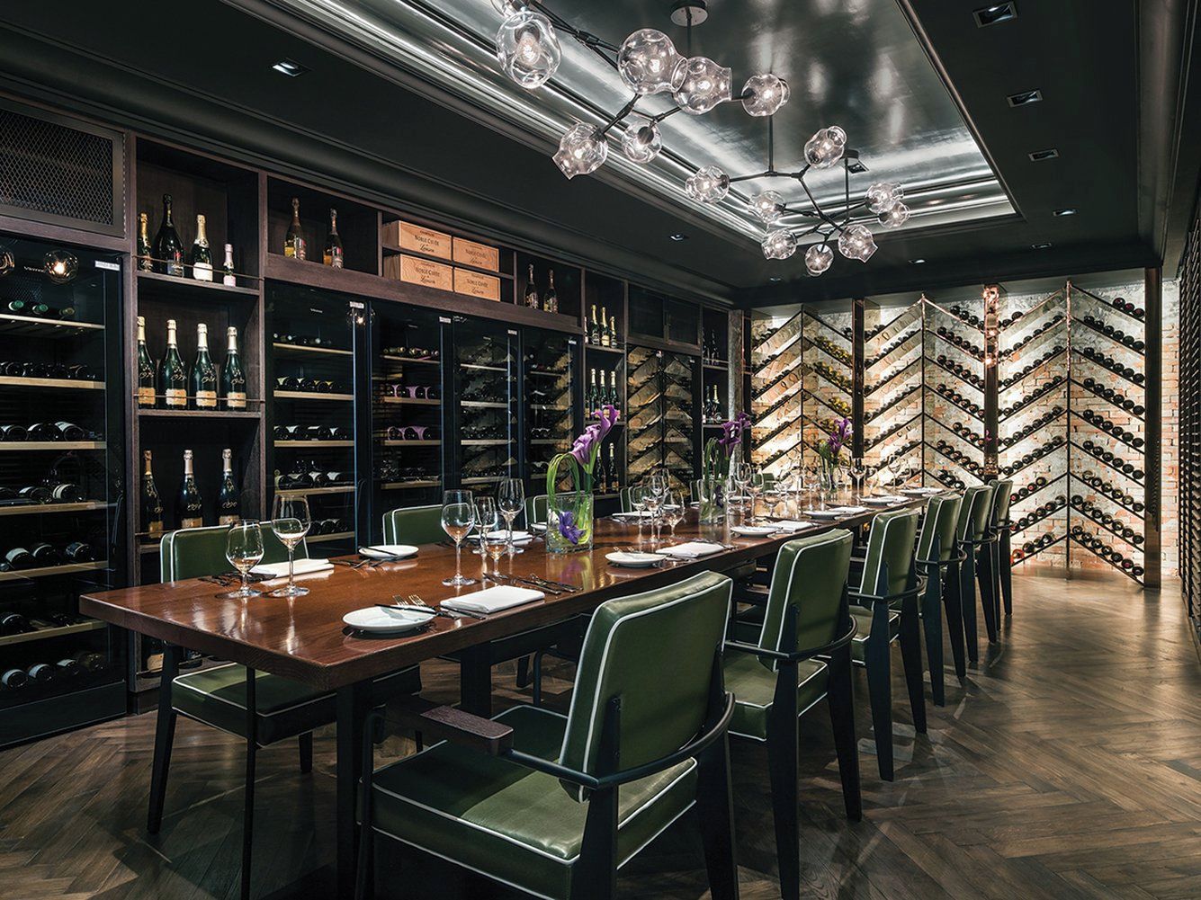 A dining area with a long table set for six, surrounded by wine racks and shelves with bottles.