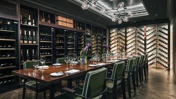 A dining area with a long table set for six, surrounded by wine racks and shelves with bottles.