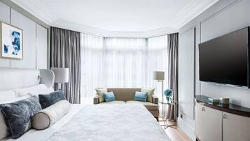 A modern hotel room with a large bed, a flat-screen TV, a seating area with a sofa, and a dining table.