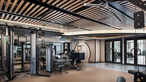 A modern gym with various exercise equipment, a bench, and a large window providing natural light. - The Langham, Hong Kong (Kowloon)