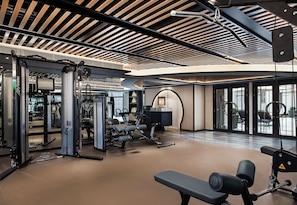 A modern gym with various exercise equipment, a bench, and a large window providing natural light. - The Langham, Hong Kong (Kowloon)