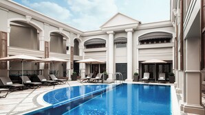 A swimming pool with lounge chairs and umbrellas, surrounded by a building with classical architecture.