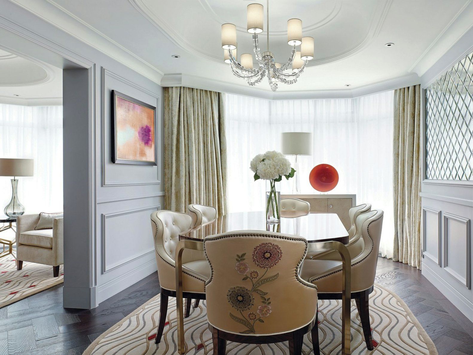 A formal dining room with a chandelier, a table, chairs, and a vase with flowers.
