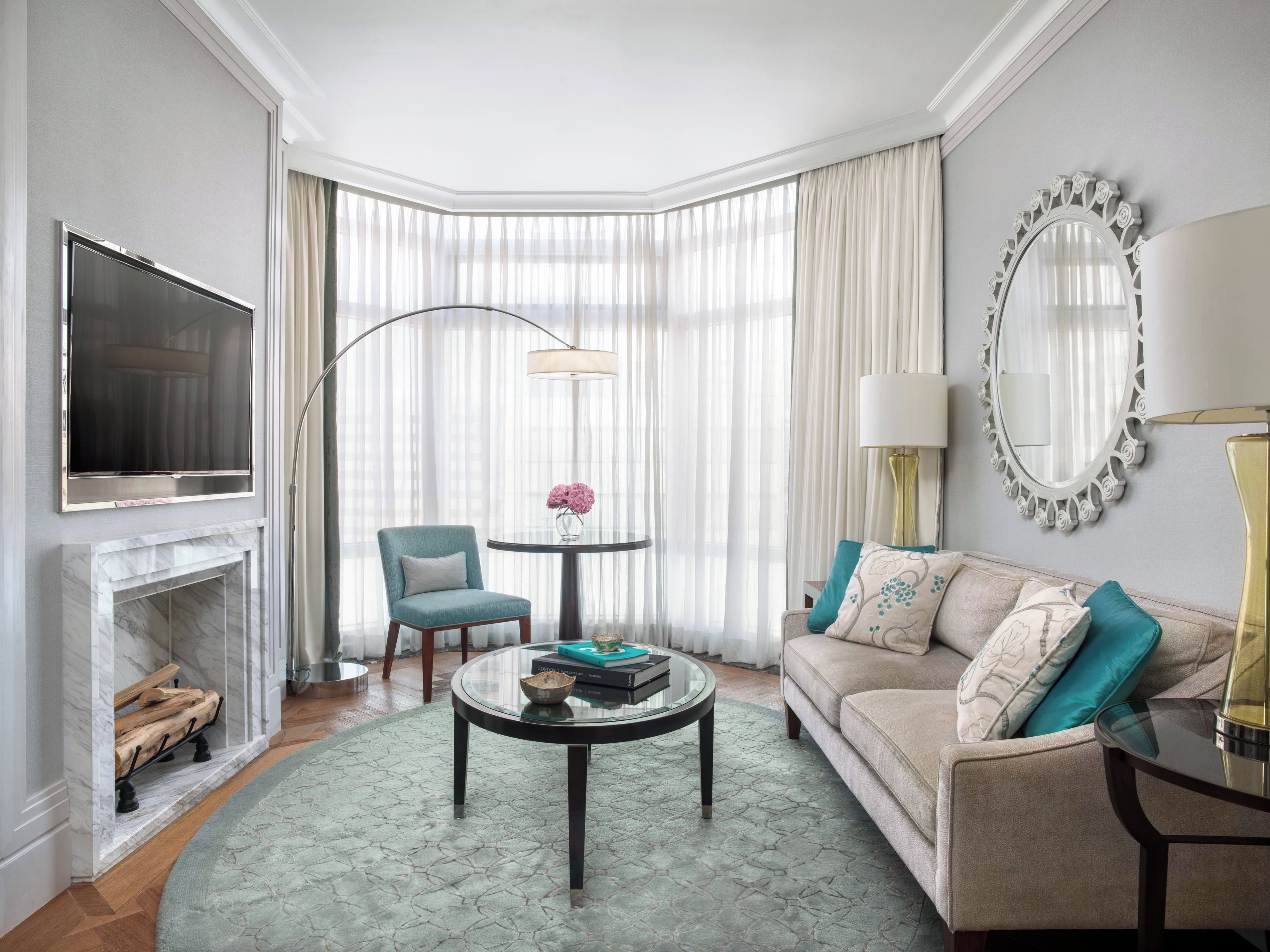 A modern living room with a fireplace, a television, a round coffee table, a sofa, and a large window with curtains.