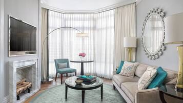 A modern living room with a fireplace, a television, a round coffee table, a sofa, and a large window with curtains.