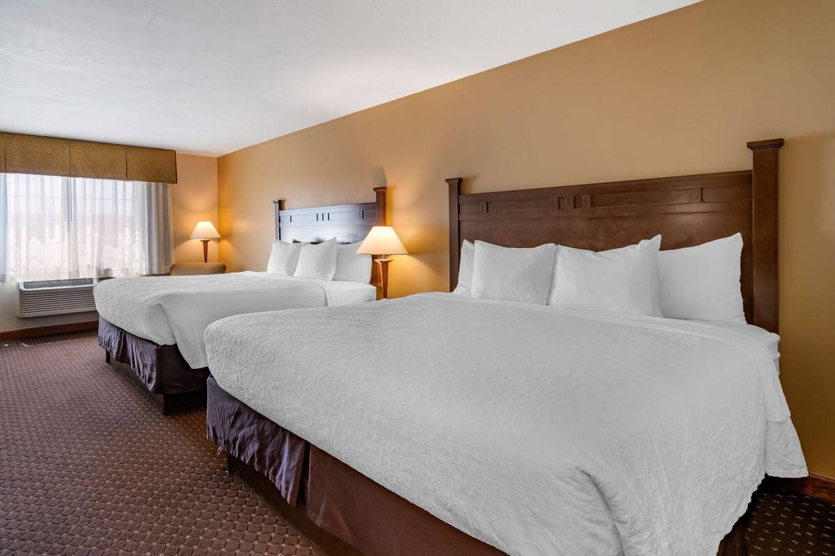 A hotel room with two beds, a large window with curtains, and two bedside lamps.