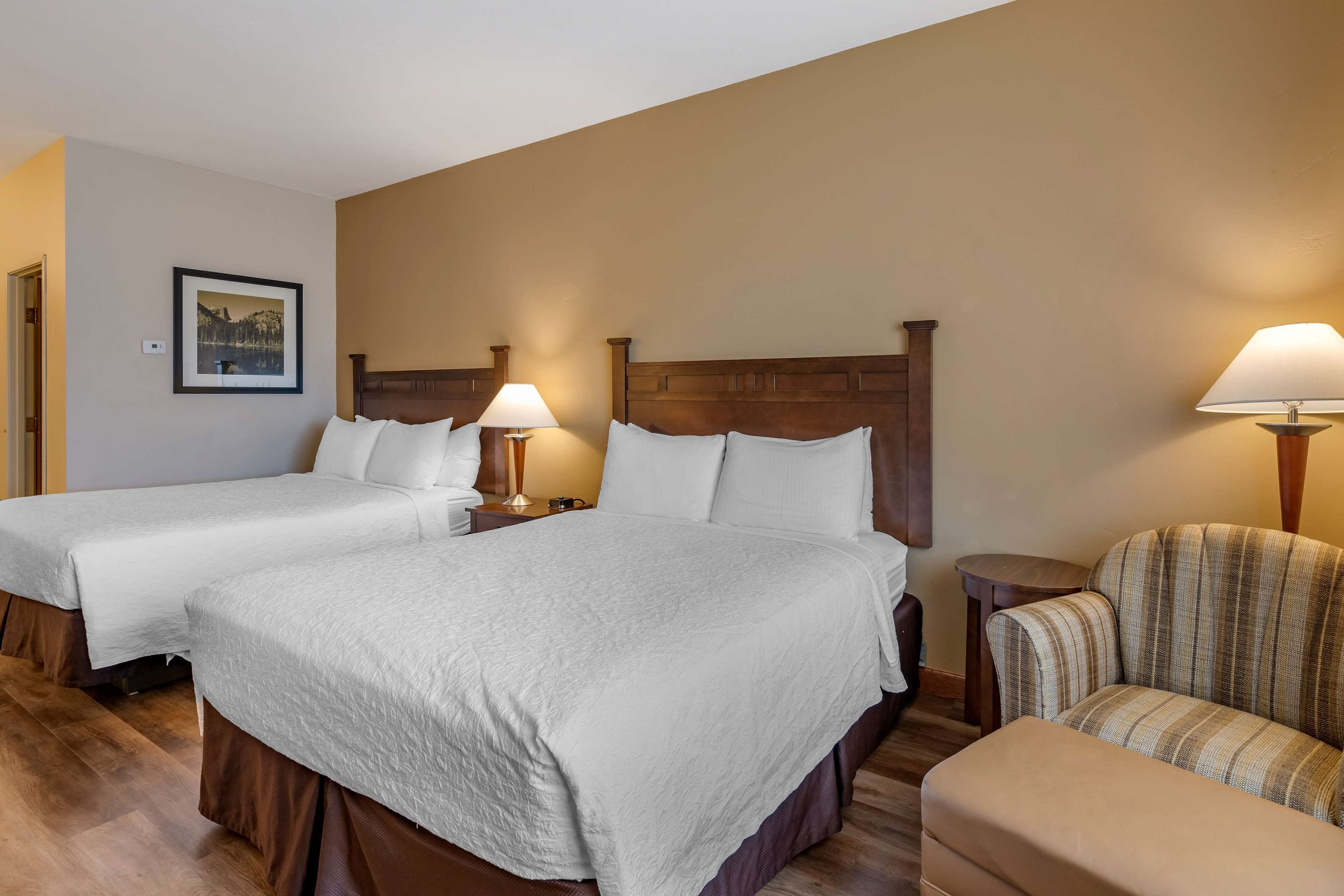 A hotel room with two beds, a chair, and a small table.