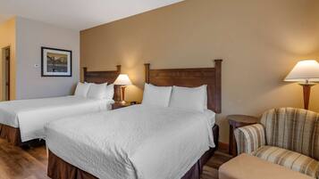 A hotel room with two beds, a chair, and a small table.