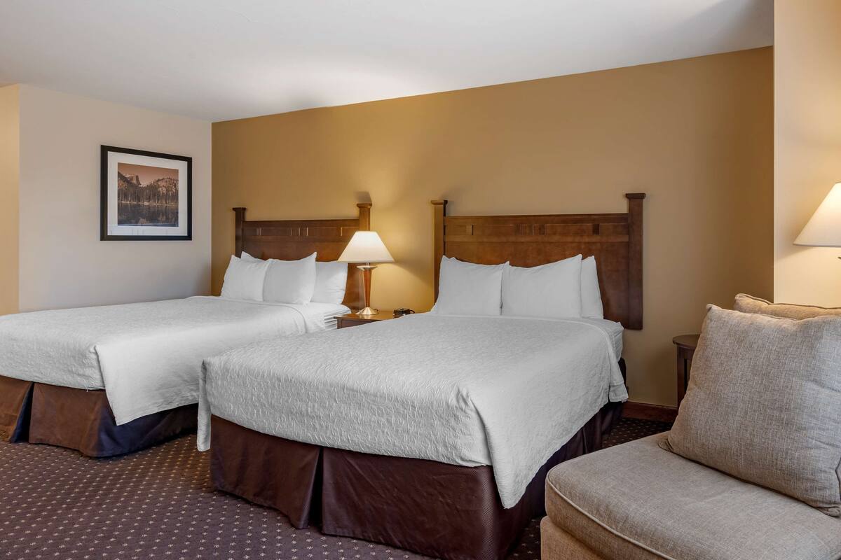 A hotel room with two beds, a chair, and a framed picture on the wall.