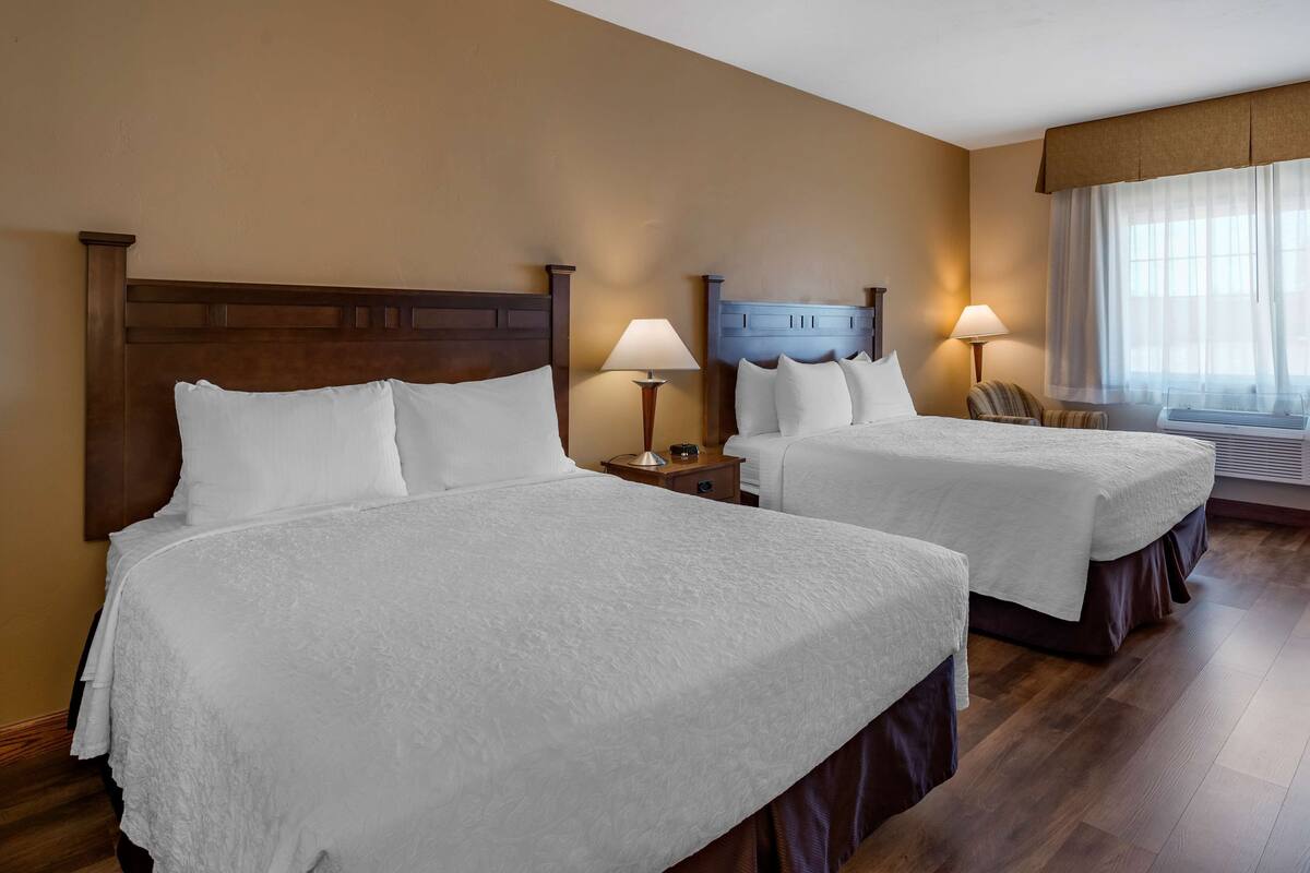 A hotel room with two beds, wooden headboards, and a large window with sheer curtains.