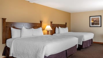 A hotel room with two beds, a wooden headboard, a nightstand with a lamp, and a framed picture on the wall.