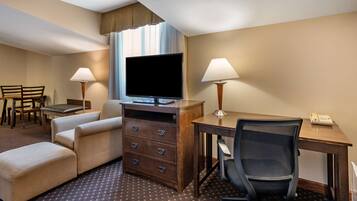 A hotel room with a flat-screen TV, two bedside lamps, a desk with a telephone, a chair, a sofa, and a dresser.
