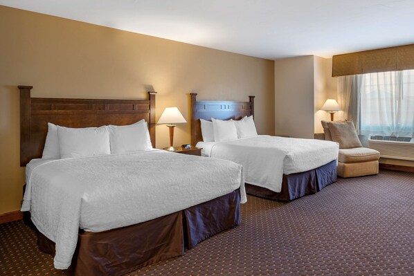 A hotel room with two beds, a chair, and a window with curtains. - Best Western Desert Inn (West Yellowstone)
