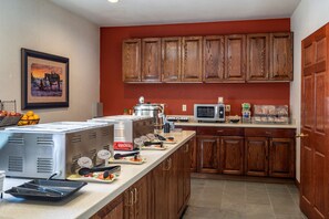 A kitchen with wooden cabinets, a microwave, and a buffet setup with various food items. - Best Western Desert Inn (West Yellowstone)