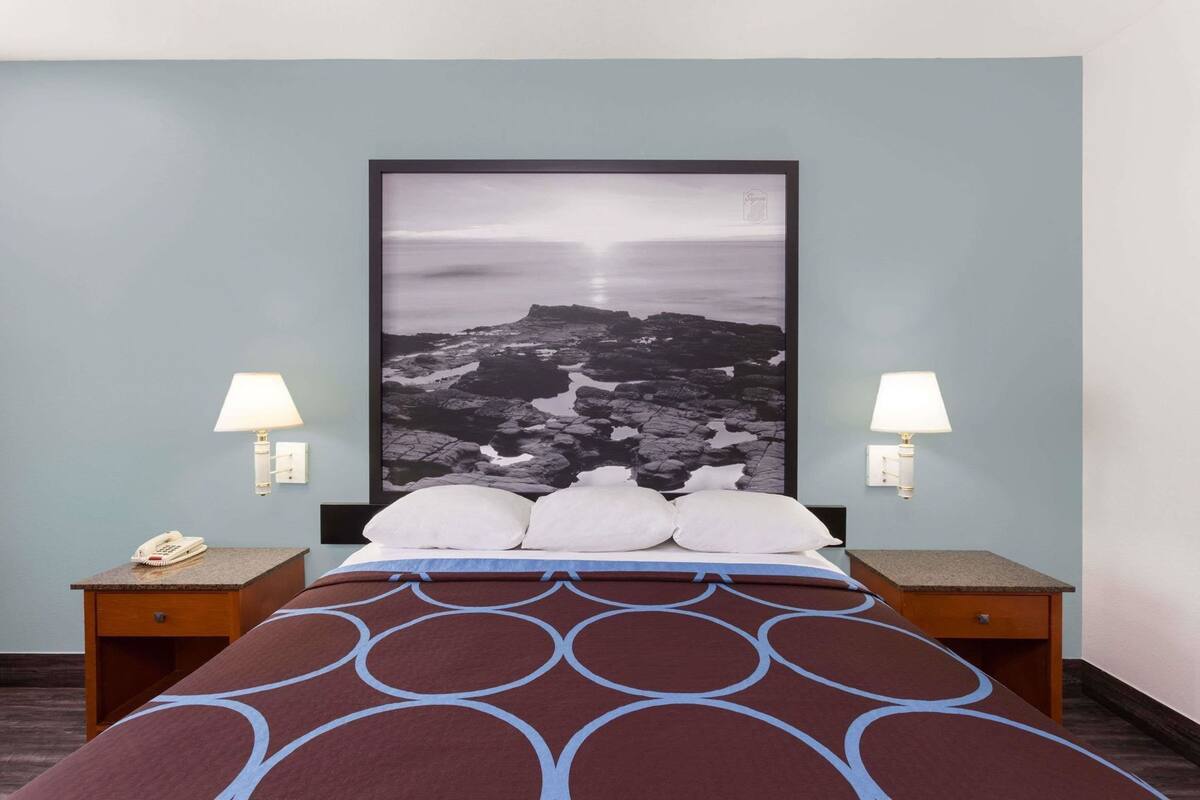 A hotel room with a bed, two bedside tables, a telephone, and a large framed picture on the wall.