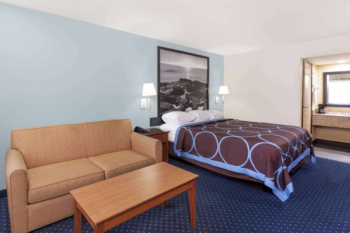 A hotel room with a bed, a sofa, a nightstand, and a desk.
