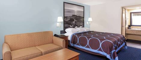 A hotel room with a bed, a sofa, a nightstand, and a desk.