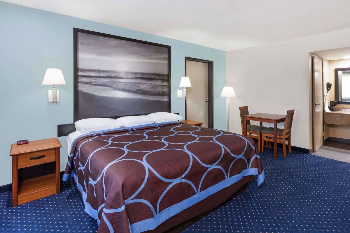 A hotel room with a large bed, a desk, two lamps, and a bathroom visible through an open door.