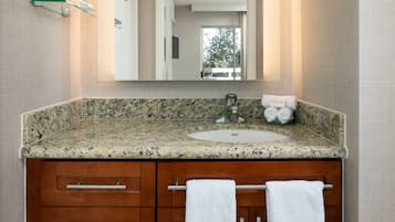A bathroom with a granite countertop, a sink, a mirror, and wooden cabinets.