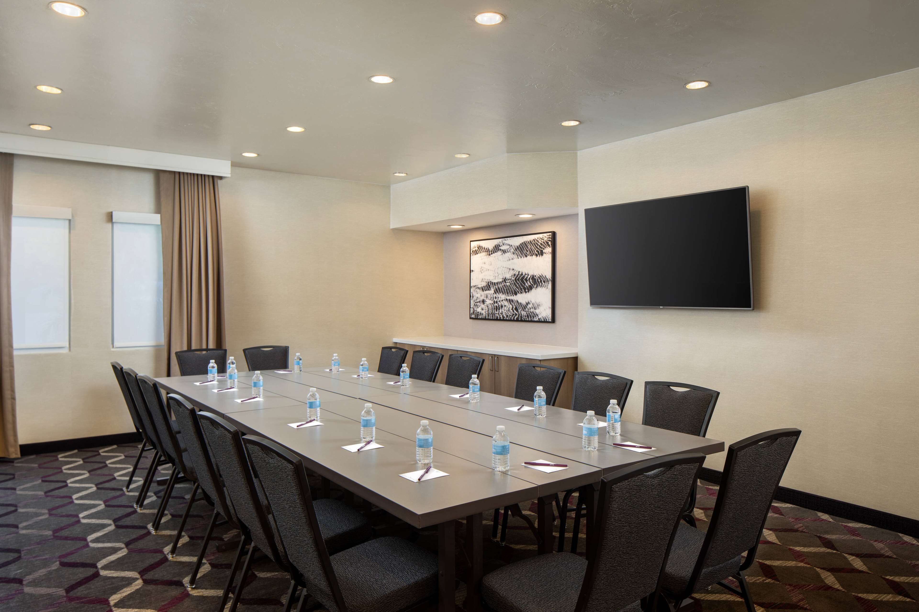 Une salle de conférence avec une longue table, des chaises, des bouteilles d’eau et un téléviseur fixé au mur.
