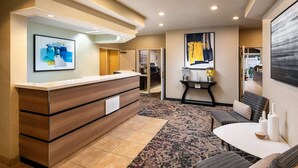 A hotel reception area with a wooden reception desk, a patterned carpet, and a seating area with a table and chairs. - Sonesta ES Suites Carmel Mountain – San Diego (San Diego)