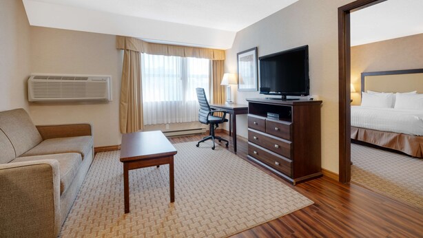 A hotel room with a sofa, a desk with a chair, a TV, a dresser, and a bed. - Best Western Plus Emerald Isle Hotel (Sidney)