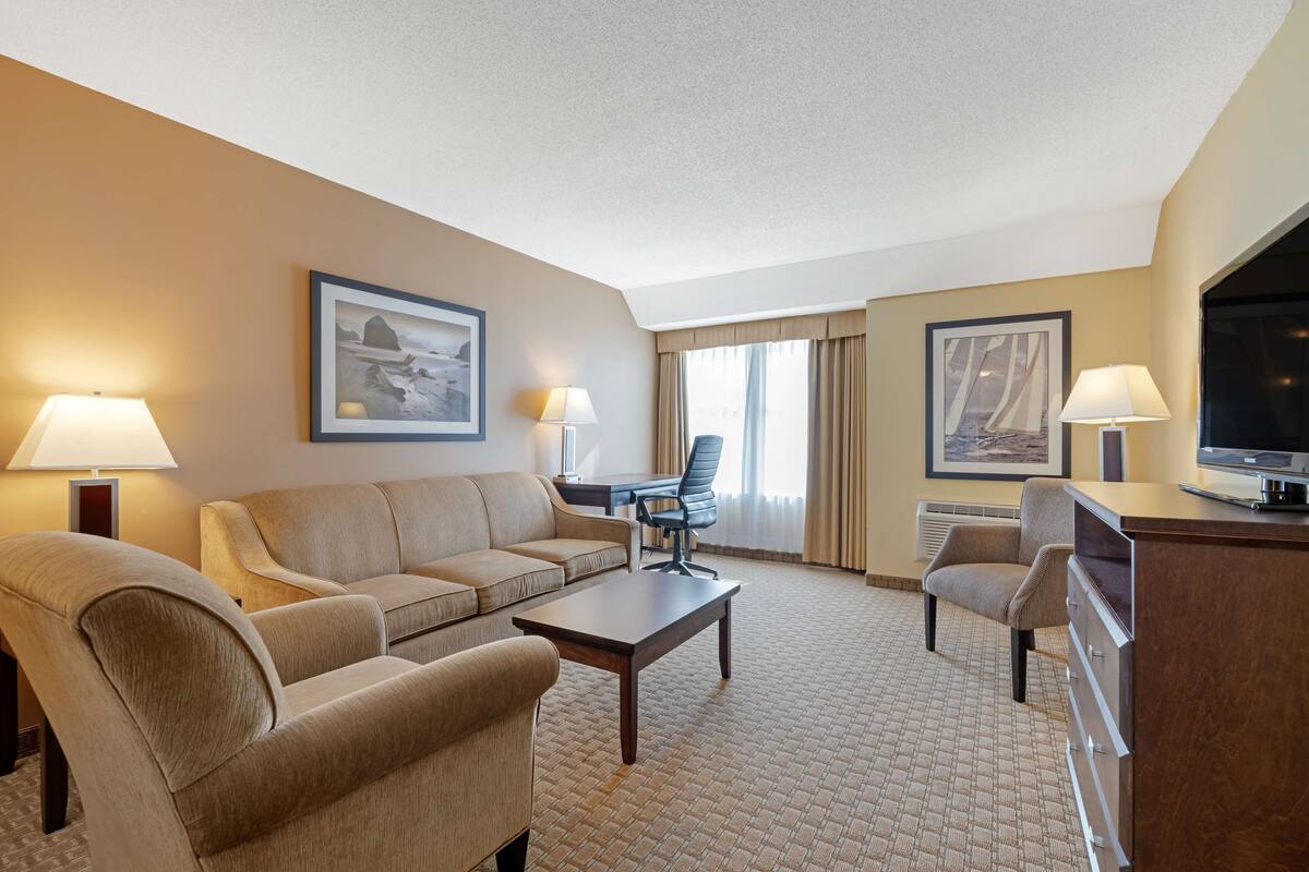A hotel room with a sofa, armchair, desk, and television.