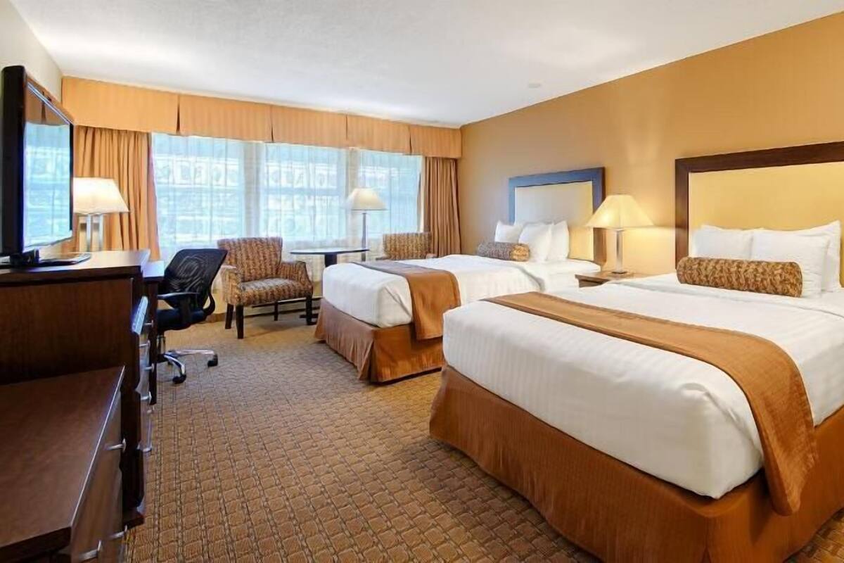 A hotel room with two beds, a desk, a chair, and a window with curtains.