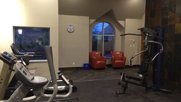 A gym with treadmills, a stationary bike, and weight machines. There is a clock on the wall and a window with a view of the outside.
