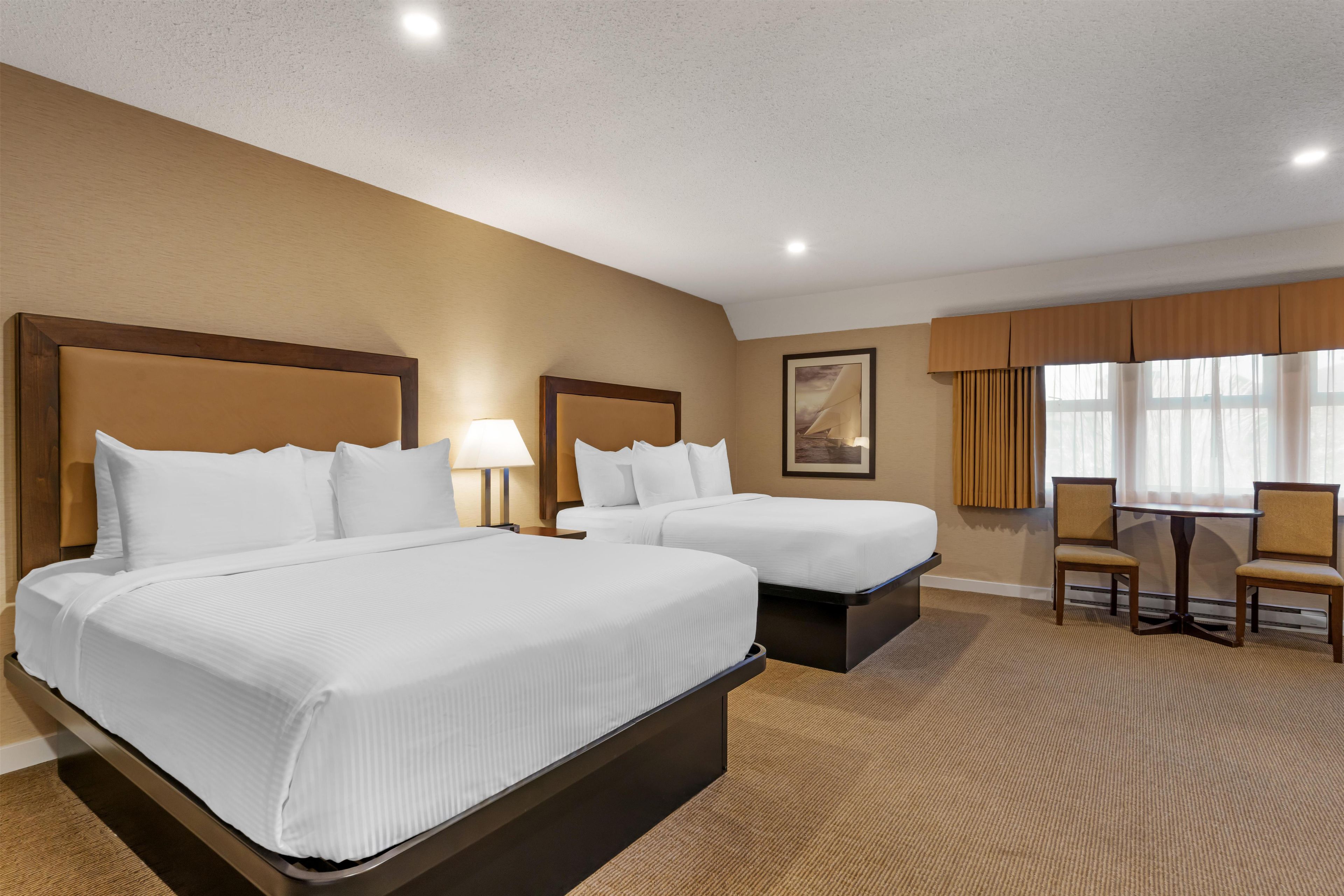 A hotel room with two beds, a desk, chairs, and a large window with curtains.