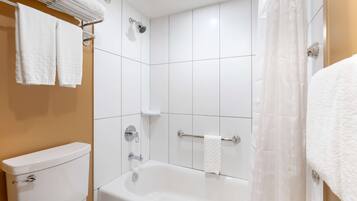 A bathroom with a white bathtub, a toilet, and a towel rack with towels.