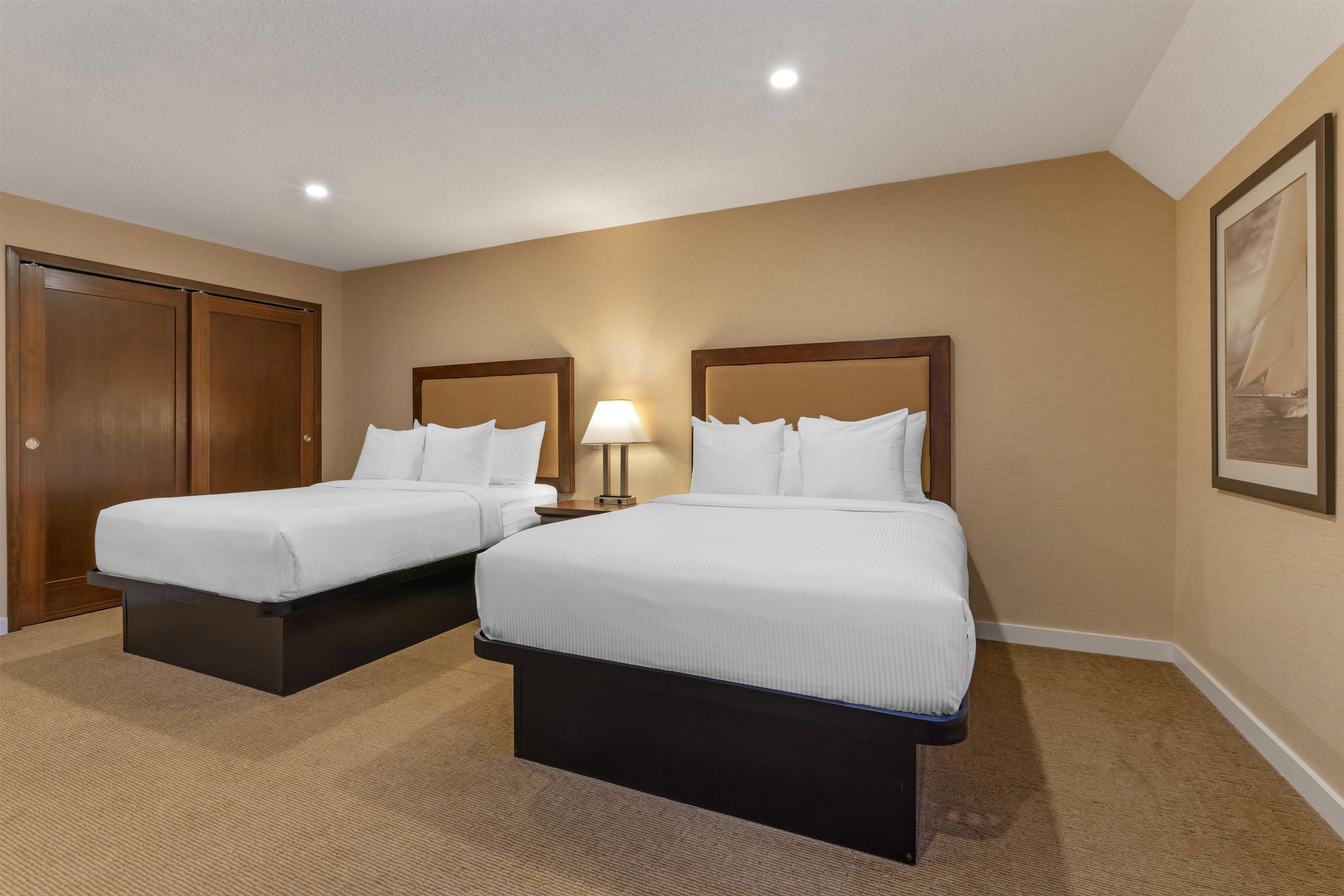Een hotelkamer met twee bedden, een nachtkastje met lamp, een houten garderobe en een lijst met een afbeelding aan de muur.
