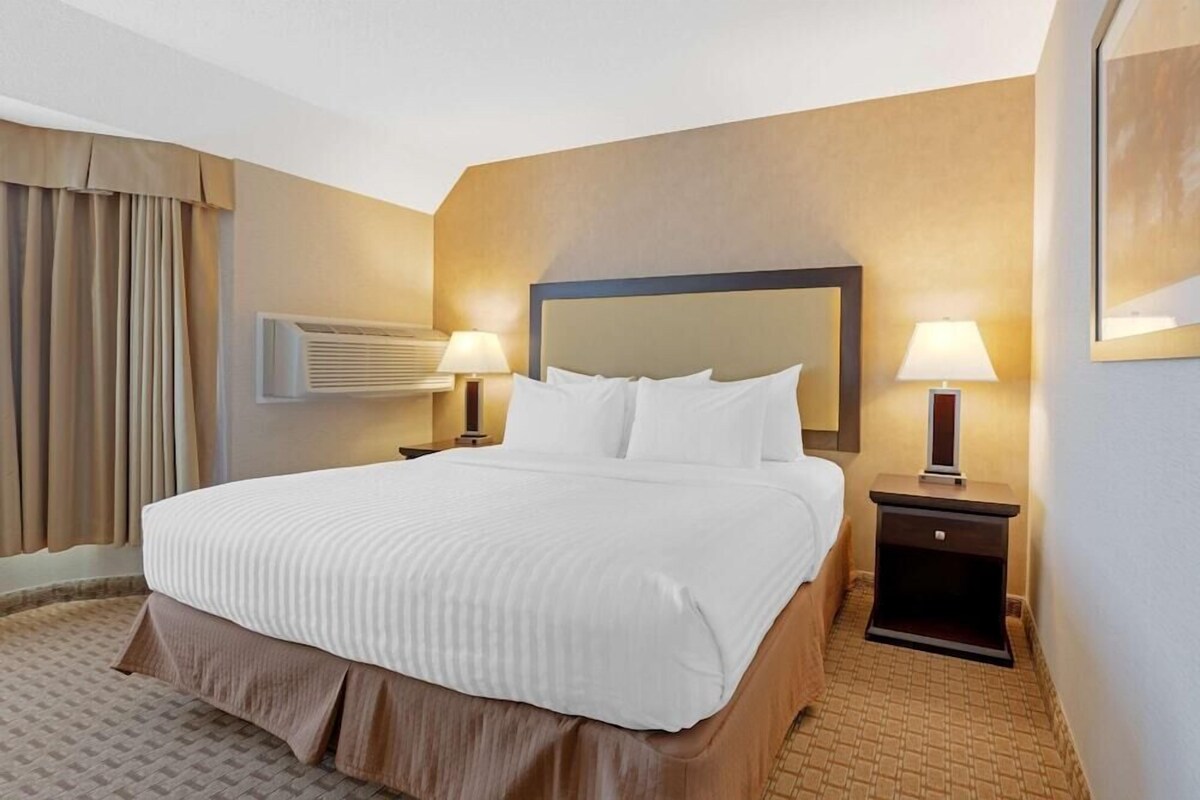 A hotel room with a large bed, two bedside tables with lamps, a wall-mounted air conditioner, and a large mirror.
