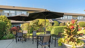 Un patio al aire libre con mesa y sillas, un gran paraguas y plantas en macetas.