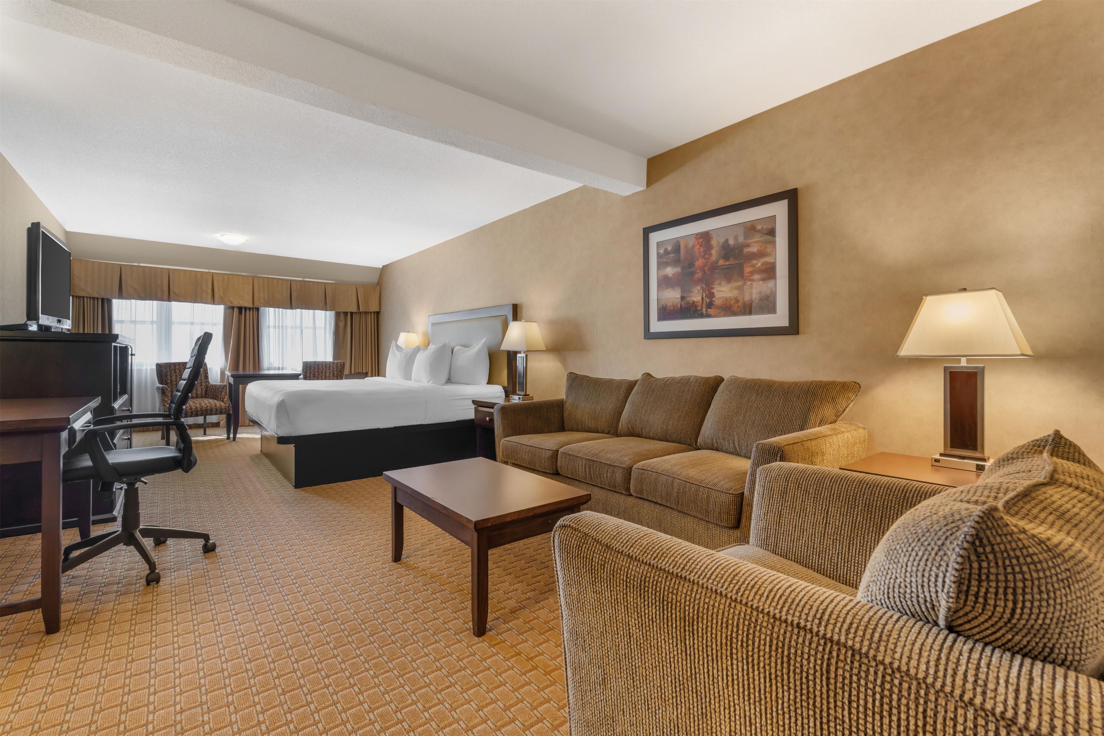 A hotel room with a bed, two sofas, a desk, a chair, a TV, and a painting on the wall.