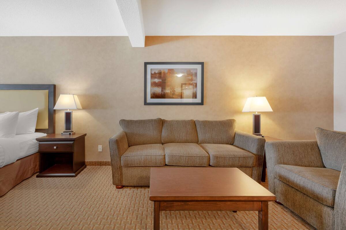 A hotel room with a bed, a sofa, a small table, and two lamps.