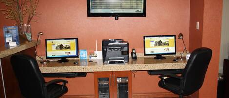 A reception desk with two computer monitors, a printer, and two office chairs.